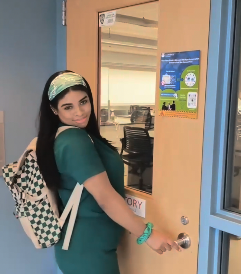 Science student in scrubs smiling in front of her classroom door
